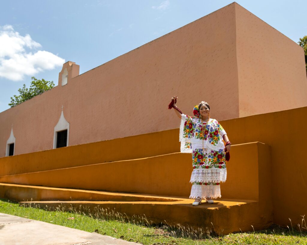 A woman in vibrant traditional attire poses outside a historic building in Mérida, Mexico.