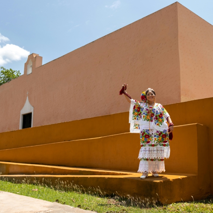 A woman in vibrant traditional attire poses outside a historic building in Mérida, Mexico.